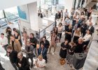 Blick von oben auf Menschen, die bei der Ausstellungseröffnung Architektouren im Foyer stehend Vorträge anhören