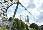 Auf diesem Bild ist das Dach im Olympiapark zu sehen. Im Hintergrund sind Bäume und ein Himmel mit Wolken zu sehen. 