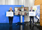 Gruppenbild der vier rezertifizierten fahrradfreundlichen Kommunen  (am Bildschirm) mit Bayerns Verkehrsministerin Kerstin Schreyer und AGFK-Vorsitzendem Matthias Dießl, die jeweils mit einem Gratulationsschild links und rechts vom Bildschirm stehen 