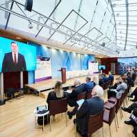 Verkehrsminister Christian Bernreiter ist auf einer Leinwand zu sehen. Die Leinwand ist vor Publikum aufgebaut, das in einem Veranstaltungsraum sitzt.