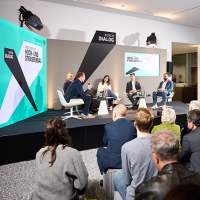 Blick auf eine Bühne, auf der eine Podiumsdiskussion stattfindet Blick auf eine Bühne, auf der eine Podiumsdiskussion stattfindet
