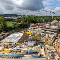 Blick über die Baustelle nach Westen. Im Vordergrund ist das fertige Untergeschoss des Parkdeck- und Kantinengebäudes, anschließend der Tiefgaragen-Verbindungsbau (Schalarbeiten) und dahinter das künftige Hauptgebäude des Neubaukomplexes zu sehen.